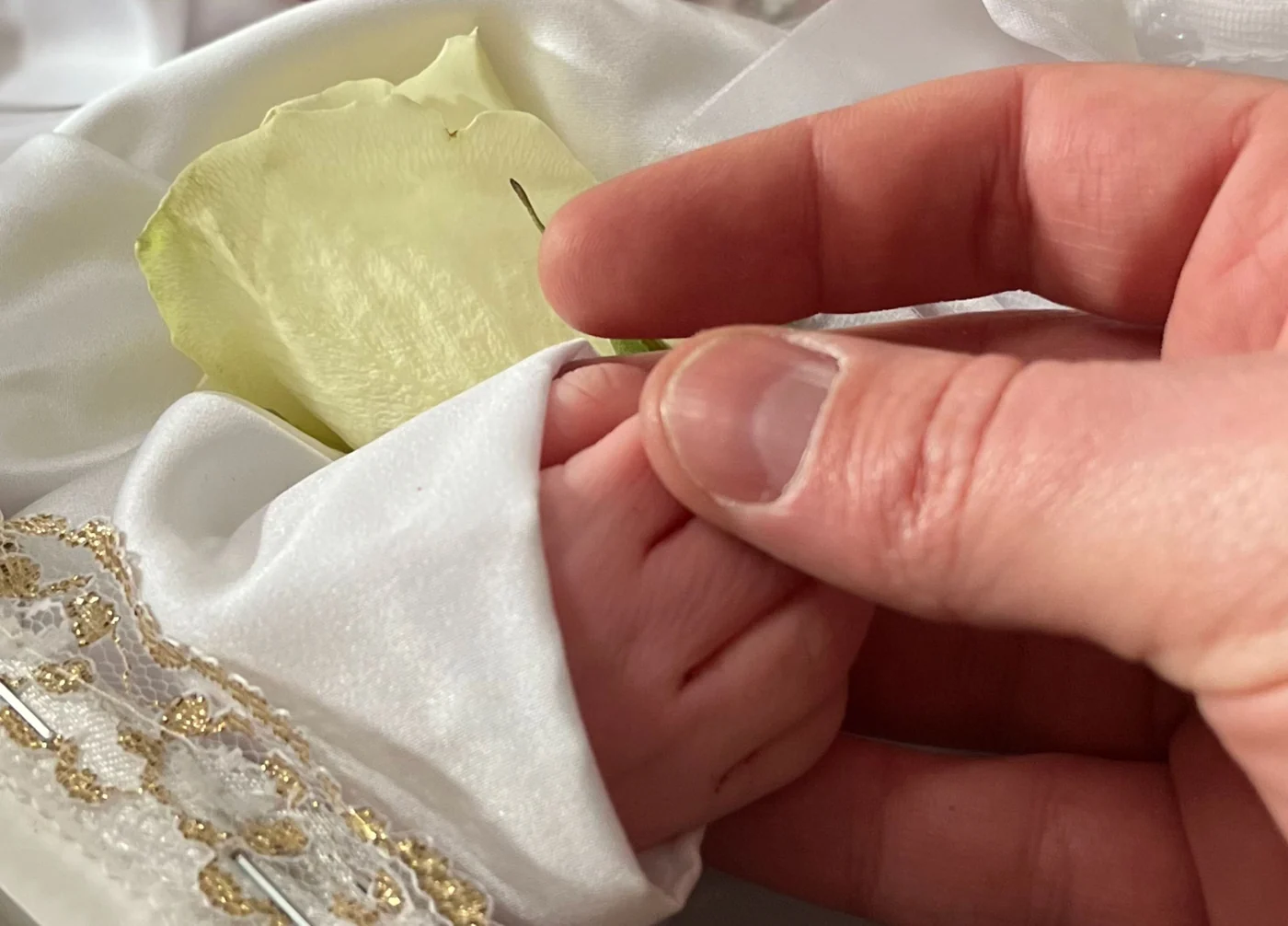 Dłoń taty trzymająca malutką rączkę Poli w rękawku białej sukienki. Obok leży biała róża.